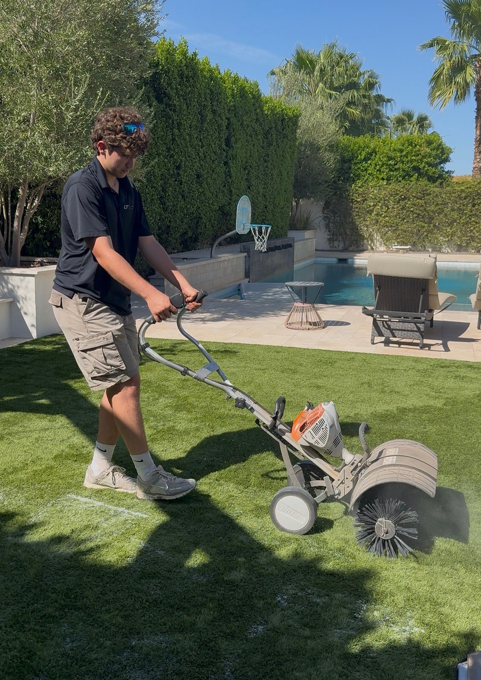 Life Turf crew power brooming artificial turf beside a backyard pool in Arizona